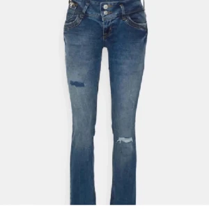 Blå bootcut jeans - Snygga blå bootcut jeans med slitningar på låren och knäna. De har en klassisk femficksdesign och är perfekta för en avslappnad stil. Jeansen har en lågmidjad passform och stängs med dragkedja och knapp.