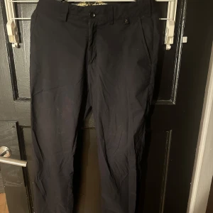 Svarta byxor från Peak Performance - Snygga svarta byxor från Peak Performance med en stilren design. Byxorna har en knapp och dragkedja framtill samt diskreta fickor bak. Perfekta för en avslappnad men ändå uppklädd look.