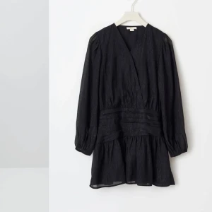 Svart omlottklänning glitter  - Snygg svart omlottklänning med v-ringad hals och långa ärmar. Klänningen har en volangdetalj vid nederkanten och en markerad midja som ger en smickrande silhuett. Perfekt för en stilren look. Den är även lite glittrig vilket för den ännu mer elegant💕Använd 1 gång, slut på Gina tricot hemsida i storlek 158/164💕