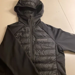 Svart jacka från Peak Performance - Säljer en svart jacka från Peak Performance med huva och dragkedja. Jackan har en quiltad design på framsidan och baksidan, vilket ger extra värme och stil. Perfekt för kyligare dagar. Den är knappt använd och såklart kan pris diskuteras vid en snabb affär!
