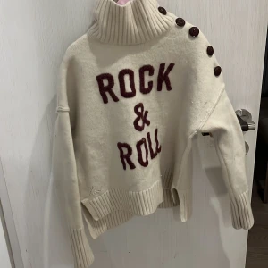 Vit rock and roll  från Zadig & Voltaire - Snygg vit polotröja från Zadig & Voltaire med texten 'Rock & Roll' i röd färg på framsidan. Tröjan har långa ärmar och knappar längs axeln för en cool detalj. Perfekt för en avslappnad och stilren look.