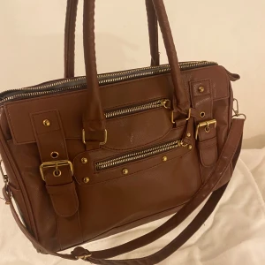 Väska - Supersnygg brun väska med gulddetaljer. Är mycket bra sick, förutom att dragkedja är lite trög. Kommer tyvärr inte ihåg vart den är köpt. 🤎