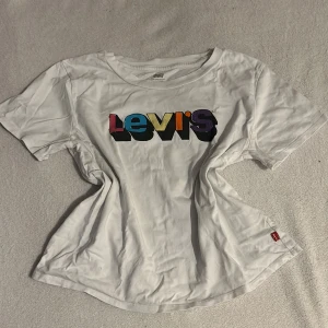 Vit t-shirt från Levi's med färgglad logga - Säljer en vit t-shirt från Levi's med en färgglad logga på bröstet. T-shirten har en rund halsringning och korta ärmar. Perfekt för en avslappnad stil. 🌈