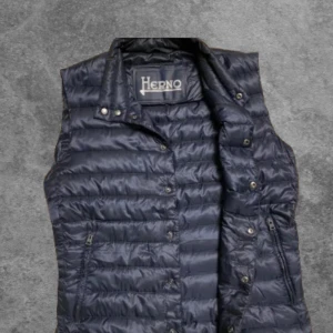 Mörkblå dunväst från Herno - Snygg mörkblå dunväst från Herno med dragkedja och knappar. Perfekt för kyligare dagar med sin quiltade design och höga krage. Nypris: 4200kr mitt pris :1299kr. Storlek S med slim fit. Ny skick. 