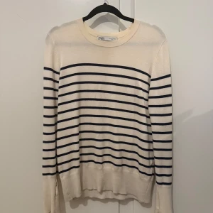 Randig tröja från Zara - Säljer en stilren randig tröja från Zara i beige och marinblått. Tröjan har långa ärmar och dekorativa knappar vid ärmsluten. Perfekt för en avslappnad look. Två hål vid armen, se bild. Om det önskas kan jag såklart sy ihop det innan tröjan skickas. Nypris 299kr mitt pris 180kr. 