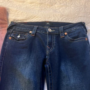 Mörkblå jeans från True Religion - Snygga mörkblå jeans från True Religion med klassiska femficksdesign och kontrastsömmar. Byxorna har en bootcut-stil och är dekorerade med knappar på bakfickorna. Jag säljer dessa då dem är för stora i midjan.