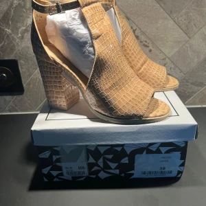 Beige klackar/sandaler från Tiamo - Snygga beige klackskor med krokodilmönster och öppen tå. Skorna har en bred klack och justerbart spänne runt ankeln. Perfekta för att ge en stilfull touch till din outfit. Sommarens Dansa-Hela-Natten-Lång klackar! Aldrig använda, endast provade.  Nypris 699:-  Se även min andra annons där jag säljer de i svart.