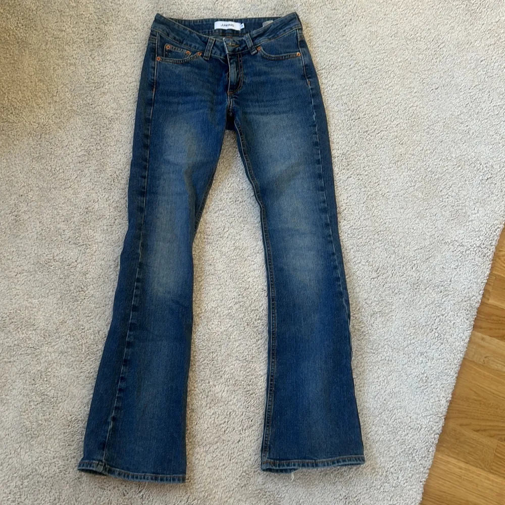 Snygga blå bootcut jeans med klassisk femficksdesign och orange sömmar. Perfekta för en avslappnad stil. De har en knapp och dragkedja framtill.. Farkut & Housut.