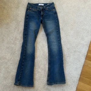 Blå bootcut jeans - Snygga blå bootcut jeans med klassisk femficksdesign och orange sömmar. Perfekta för en avslappnad stil. De har en knapp och dragkedja framtill.