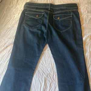 Mörkblå jeans  - Snygga mörkblå jeans med flare ben och klassisk femficksdesign. De har kontrasterande sömmar och knappar i metall. Perfekta för en avslappnad stil.