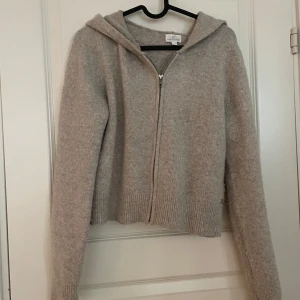 Beige stickad hoodie med dragkedja - Mysig beige stickad hoodie med dragkedja framtill. Tröjan har långa ärmar och en huva, perfekt för kyliga dagar. Ribbstickade muddar vid ärmslut och nederkant ger en skön passform. Använd endast 3 gånger💕