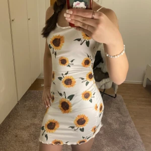 Vit klänning med solrosmönster - Säljer en superfin vit klänning med solrosmönster. Klänningen är ärmlös och har en tight passform som framhäver figuren. Perfekt för sommarens alla tillfällen! 🌻