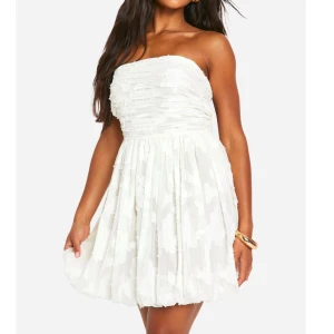 Vit axelbandslös klänning - Säljer denna oanvända vita axelbandslös klänning med volangdetaljer och knytning i ryggen. Perfekt för sommarens festligheter. Klänningen har en kort längd och ett fint mönster 😊priset kan diskuteras. 