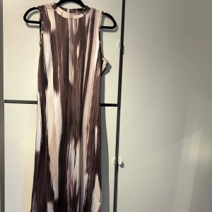 Mönstrad ärmlös klänning - Säljer en cool ärmlös klänning med ett abstrakt mönster i bruna och beige toner. Klänningen har en lång passform och rund halsring