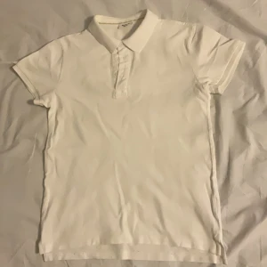 Vit pikétröja från Kappahl - Säljer en klassisk vit pikétröja från Kappahl i storlek 158/164. Tröjan har korta ärmar och en stilren krage med knappar framtill. Perfekt för en avslappnad och stilren look.