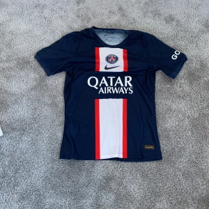 Blå psg fotbollströja från Nike  - Säljer en blå fotbollströja från Nike med vit och röd detalj på framsidan. Tröjan har korta ärmar och Qatar Airways-logga på bröstet. Perfekt för fotbollsfans!