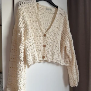 Vit stickad kofta från Pull&Bear - Säljer en vit stickad kofta från Pull&Bear med ett luftigt mönster och tre knappar framtill. Koftan har en croppad passform och långa ärmar, perfekt för lager-på-lager-stil. 🧶✨