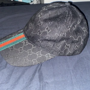 Svart keps med mönster och randig detalj - Snygg svart keps med diskret mönster och en randig detalj i grönt och rött på skärmen. Perfekt för en stilren look.