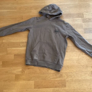 Grön/brun hoodie från Woxg - Säljer en grön/brun hoodie från Woxg med ett tryck på baksidan. Säljer dennna hoodie för att den är för liten för mig men annars så är den väldigt skön och snygg, det är inga hål men det finns några små fleckar. 