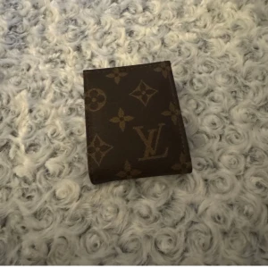 Brun plånbok  - Snygg brun plånbok  med det klassiska monogrammönstret. Plånboken har flera fack för kort och sedlar, perfekt för att hålla ordning på dina tillhörigheter. En stilren accessoar för den modeintresserade.