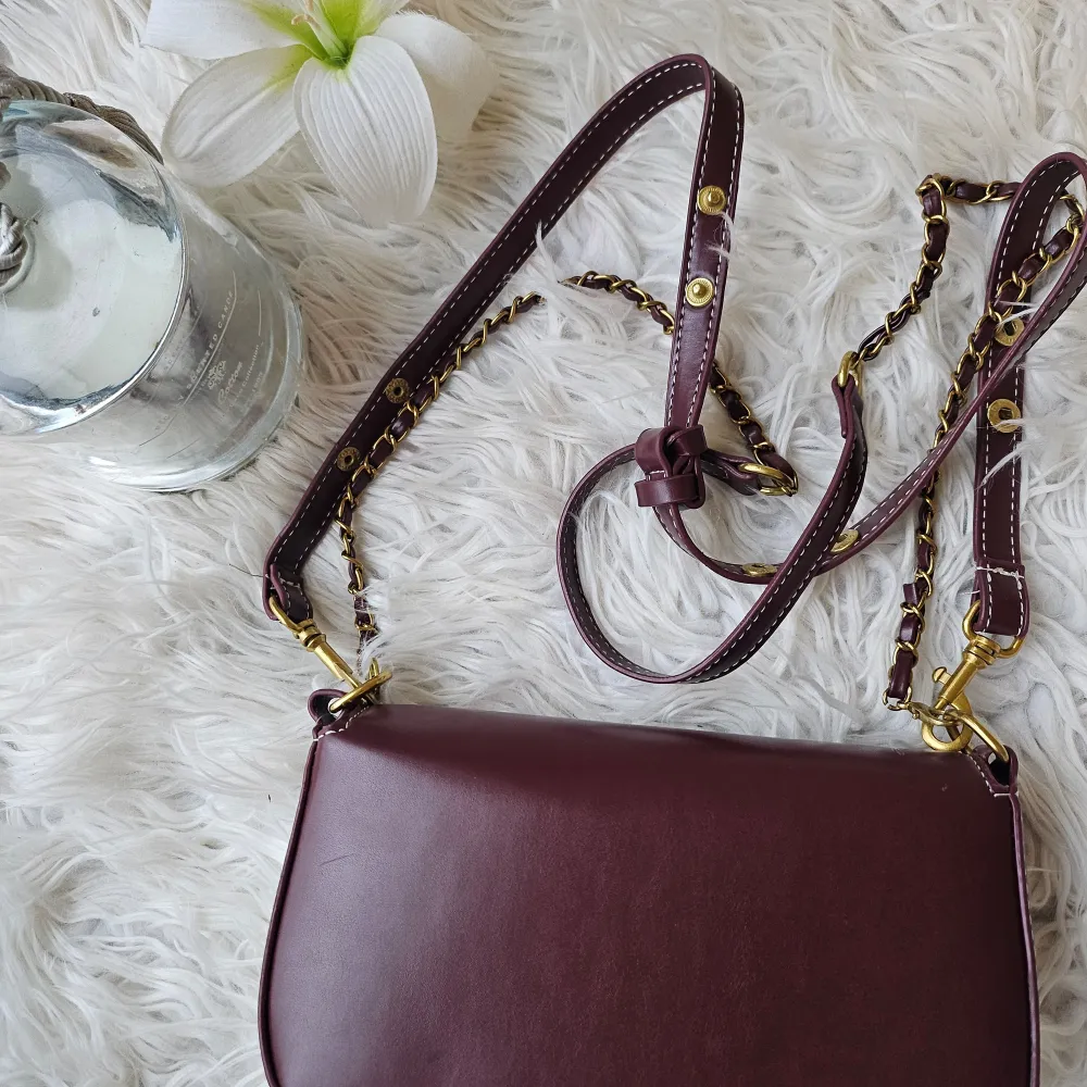 Snygg brun axelväska från Tory Burch i skinn med gulddetaljer. Väskan har en elegant kedjerem och ett stilrent spänne framtill. Perfekt för att ge din outfit en lyxig touch.. Laukut & Käsilaukut.
