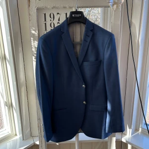 Blå kostym från Tiger of Sweden - Elegant blå kostym från Tiger of Sweden. Kavajen har två knappar och en klassisk passform med fickor fram. Byxorna är matchande och ger en stilren look. Storlek 48/48, kostymen har använts fåtal gånger och är i nyskick 