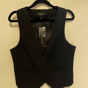 Svart väst från Attentif - Snygg svart väst från Attentif med knappar framtill. Perfekt för en stilren look. Västen har en klassisk design med en v-ringad framdel. Helt ny med lappen kvar 💕