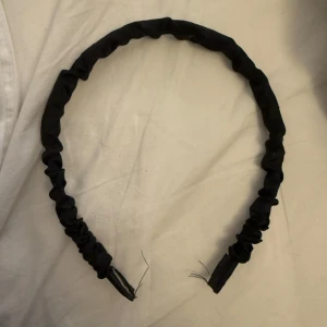 Svart diadem i tyg - Säljer ett enkelt svart diadem i tyg. Perfekt för att hålla håret på plats med stil. Diademet har en mjuk och flexibel passform.