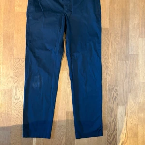 Helt nya Mörkblå byxor från J. Lindeberg - Helt nya! Snygga mörkblå byxor från J. Lindeberg i modellen Chaze Super Satin. Byxorna har en elegant finish och är perfekta för en stilren look. De har knappar bak och en klassisk passform.