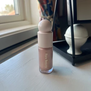 Flytande highlighter från Rare Beauty - Snygg flytande highlighter från Rare Beauty i en ljusrosa nyans. Perfekt för att ge ansiktet en strålande glöd. Kommer i en smidig flaska med en rund applikator för enkel applicering. Endast testad. Nypris: 489kr🌟 