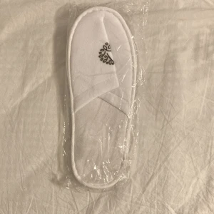 Vita spa-tofflor - Säljer ett par vita spa-tofflor med öppen tå och korsad design. Perfekta för en avslappnad dag hemma eller på spa. Tofflorna är förpackade i plast och har en mjuk känsla.