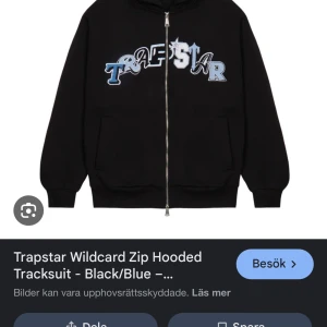 Svart huvtröja med dragkedja från Trapstar - Säljer en svart huvtröja med dragkedja från Trapstar. Tröjan har ett stort tryck i blått och vitt på framsidan. Den har långa ärmar och en bekväm passform med ribbade muddar vid ärmslut och nederkant.