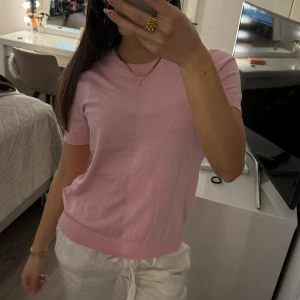 Rosa kortärmad tröja  - Säljer en söt rosa kortärmad stickad tröja. Perfekt för en avslappnad stil. Tröjan har en rund halsringning och är gjord i ett mjukt material.