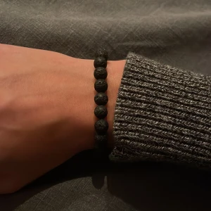 Svart armband med pärlor - Snyggt svart armband med pärlor gjorda av lavasten och en brun sten. Perfekt för att ge en stilren touch till din outfit. Elastiskt band för enkel passform.