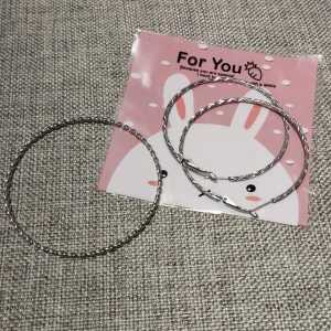 Silvriga vridna örhängen + armband  - Snygga silvriga örhängen med en vriden design. Perfekta för att ge en stilren touch till din outfit. De är lätta och bekväma att bära hela dagen. Örhängen är 6 cm i diametern.  Armbandet är 8 cm i diametern.