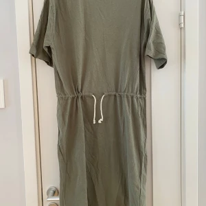 Grön klänning från Filippa K - Säljer en stilren grön klänning från Filippa K. Klänningen har korta ärmar och ett knytband i midjan för en justerbar passform. Perfekt för en avslappnad look. 💚 Ny grön klänning i strl L i bomull/linne från Filippa K.  Ny, aldrig använd.  Mått Över bröstet: ca 54 cm Längd från axeln och ner: ca 105 cm  60% bomull och 40% linne  Kommer från ett djur och rökfritt hem.