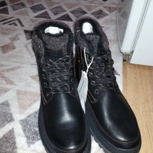 Svarta kängor från Tom Tailor - Snygga och robusta svarta kängor från Tom Tailor med snörning och vadderad krage. Perfekta för kalla dagar med slitstark sula och vattenavvisande material. Märkesdetaljer på sidan och etikett kvar. Använder inte helt nytt 