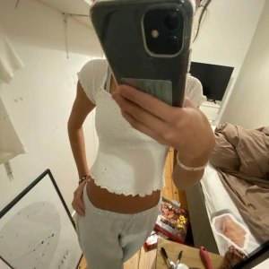 Vit topp från Stradivarius - Säljer en söt vit Stradivarius topp med smockdetaljer och korta ärmar. Toppen har en elastisk passform och en snygg vågig kant vid ärmslut och nederkant. Perfekt för en somrig look! Det är dock en väldigt liten storlek, jag tror att det också är en barnstorlek💗