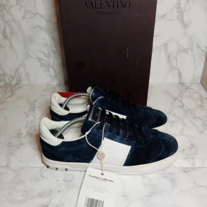 Valentino Garavani sneakers i blå mocka - Snygga Valentino Garavani sneakers i blå mocka med vita detaljer. Skorna har en unik sula med kamouflagemönster och dekorativa nitar runt hälen. Perfekta för en stilren look.