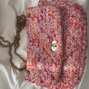 Färgglad axelväska med kedja - Snygg och färgglad axelväska i ett mönster av rosa, orange och rött. Väskan har en elegant kedja som axelrem och ett stilrent spänne framtill. Perfekt för att liva upp vilken outfit som helst!