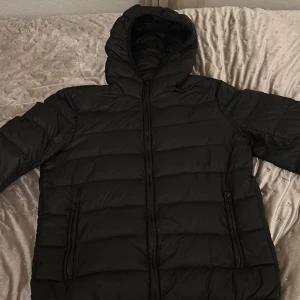 Svart pufferjacka från Zara - Säljer en svart pufferjacka från Zara med huva och dragkedja. Jackan är perfekt för kyligare väder och har en stilren design. Den är i storlek M  men passar även S. Jackan passar både för höst och vinter.