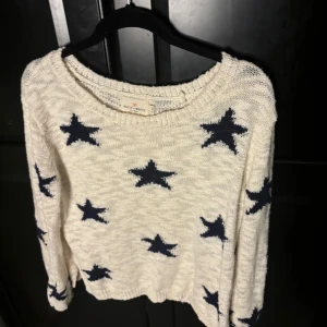 Vit stickad tröja med stjärnor - Säljer en vit stickad tröja med mörkblå stjärnor. Tröjan har en avslappnad passform och långa ärmar. Perfekt för en mysig dag.