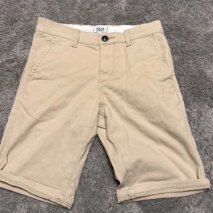 Beige shorts från Jack & Jones - Snygga beige shorts från Jack & Jones med knapp och dragkedja. Perfekta för sommardagar med sin bekväma passform och stilrena design.