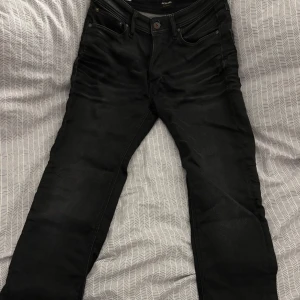 Svarta jeans från Jack & Jones - Snygga svarta jeans från Jack & Jones med en klassisk design. De har en bekväm passform och är perfekta för en stilren look. Jeansen har fem fickor och knappgylf.