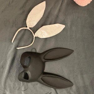 Svart mask och vitt diadem med kaninöron - Säljer en svart mask med kaninöron och ett vitt diadem med kaninöron. Perfekt för maskerad eller fest. Masken har en slät yta och diademet är enkelt och stilrent.