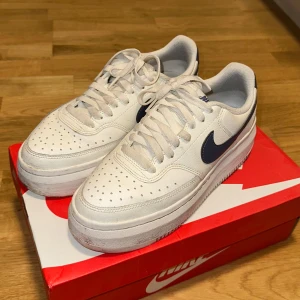 Nike air force white och blå - Säljer ett par Nike Ourt Vision Alta LTR  sneakers i vitt med blå detaljer på en bra sick. Skorna har en stilren design med snörning och en robust sula. Perfekta för en casual look. 