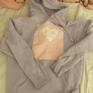 melanie martinez k-12 hoodie - Säljer en ljuslila hoodie med tryck från Melanie Martinez K-12 Tour. Tröjan har en stor ficka framtill och en luva med dragsko. På framsidan finns ett hjärtformat tryck med texten 'K-12' och på baksidan en lista över turnédatum.