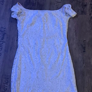 Vit spetsklänning - Elegant vit spetsklänning med korta ärmar och vackert mönster. Perfekt för sommarens festligheter. Klänningen har en figurnära passform och en klassisk design.