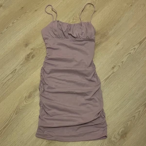 Ljuslila klänning med rynkdetaljer - Snygg ljuslila klänning med smala axelband och rynkdetaljer på sidorna. Perfekt för en stilren look.