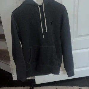 Grå hoodie från Ralph Lauren - Säljer en stilren grå hoodie från Ralph Lauren med klassisk design. Tröjan har en justerbar huva med vita snören och en känguruficka framtill. Perfekt för en avslappnad look. Inga defekter 9/10 skick. Nypris 2000kr